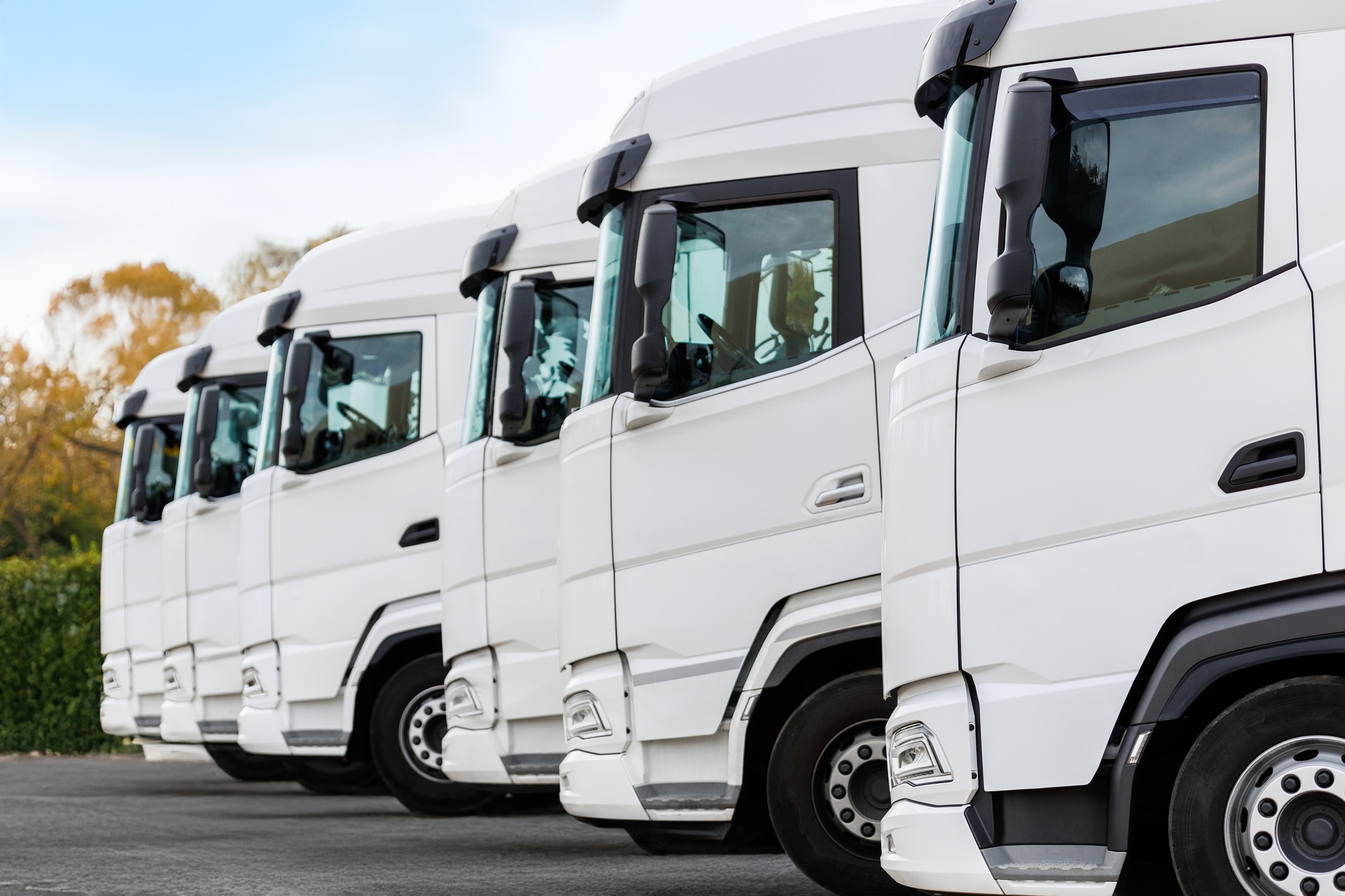 Fleet of new modern electric hybrid hydrogen or diesel white trucks parked in line row outdoors