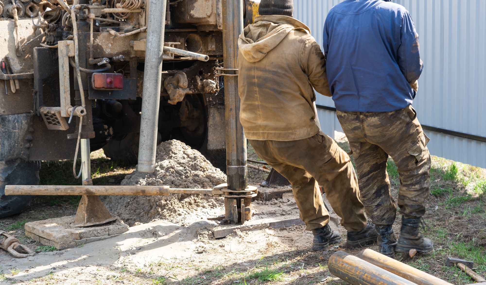 Team of workers with drilling rig on car are drilling artesian well for water in ground